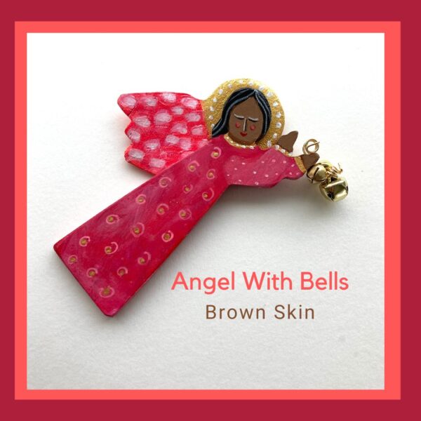 A brown skin flying wood angel ornament holding 3 bells. She is wearing a bright red and pink dress with a dot and circle pattern.