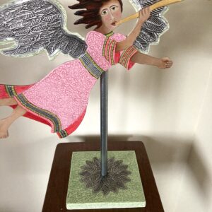 Red and pink wood flying angel with a trumpet mounted on a pole with a base. Decorative sculpture. This angel is flying left to right.