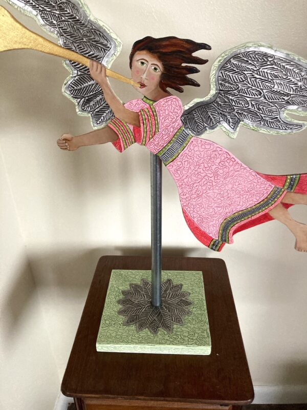 Red and pink wood flying angel with a trumpet mounted on a pole with a base. Decorative sculpture.